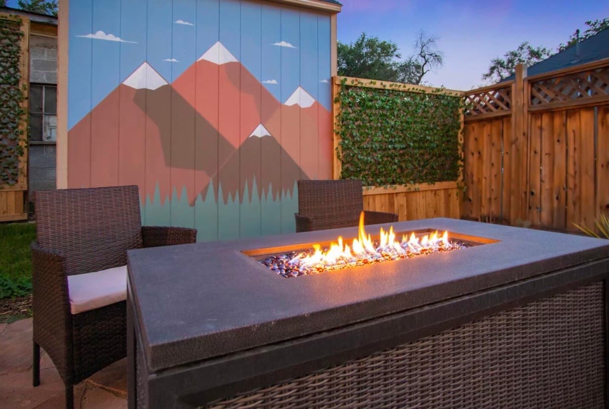 The backyard of an Airbnb rental, showing a firepit and a mural of the mountains behind it.